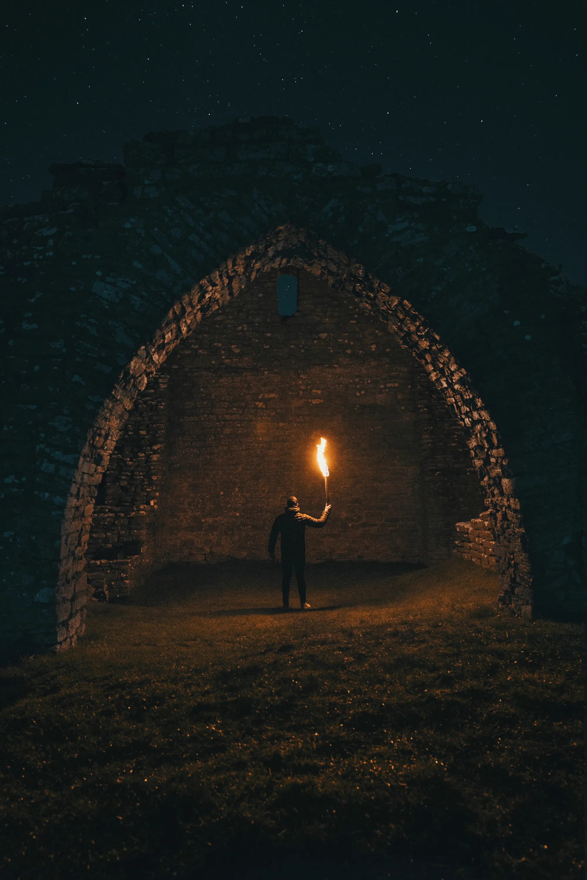 A figure holding a flaming torch in a dark stone archway